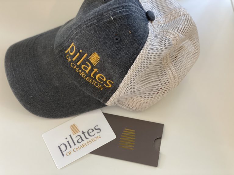Embroidered black and beige Pilates of Charleston trucker hat with branding.