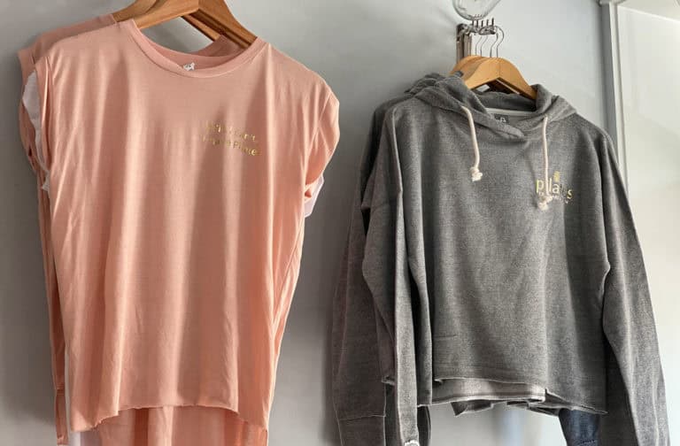 Elegant pink and gray Pilates-branded athletic apparel on hangers.