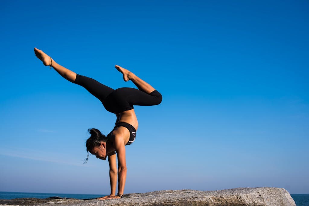 Yoga pose on rocks near ocean, outdoor fitness for balance and core strength.
