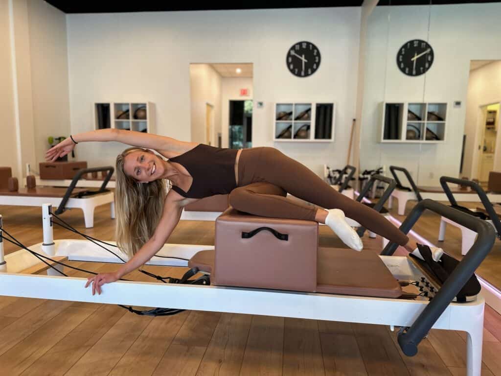 Smiling woman exercising on Pilates reformer machine at Charleston Pilates studio for fitness and flexibility.